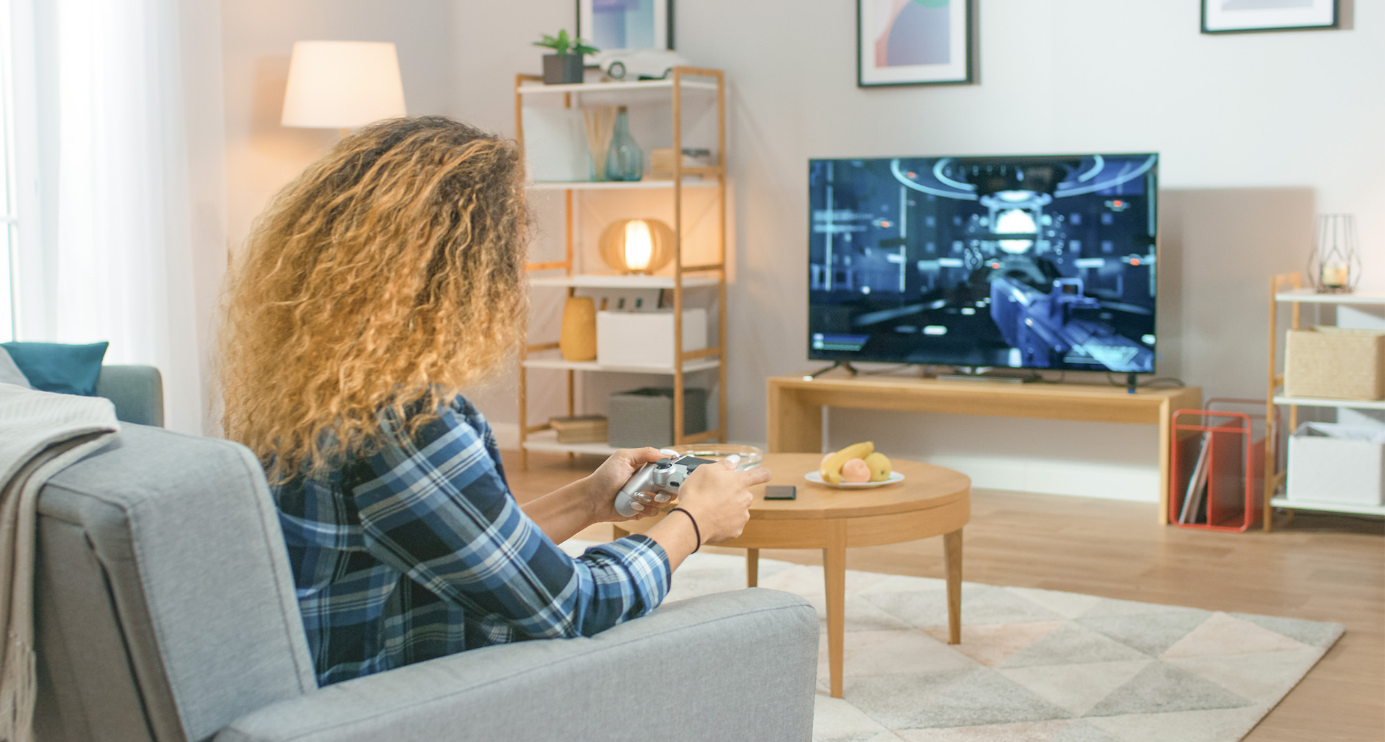 Person mit langen lockigen Haaren im Wohnzimmer, die Videospiele vor einem Fernseher spielt